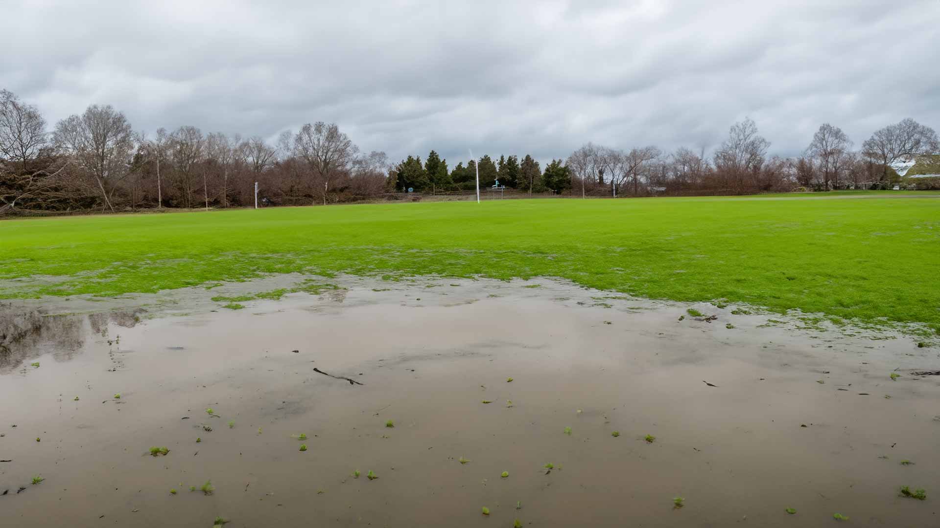 Flooded athletic field with standing water and saturated soil, posing risks to landscape health